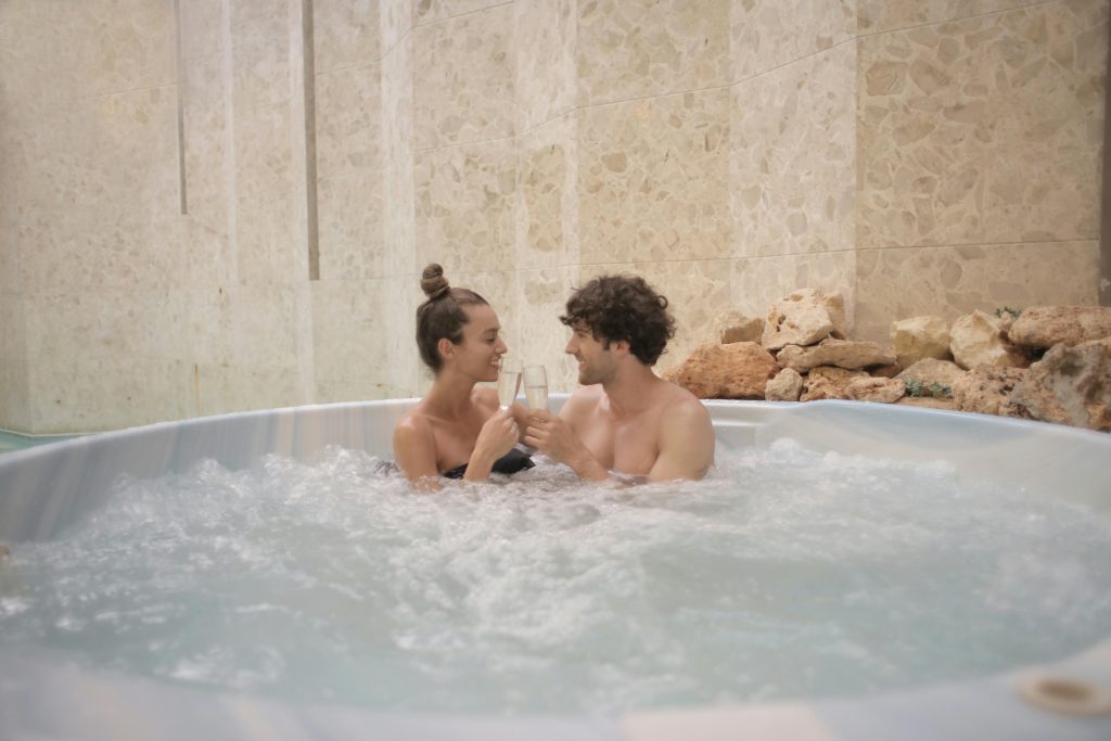 A happy couple toasting with champagne glasses in a luxurious indoor hot tub setting.