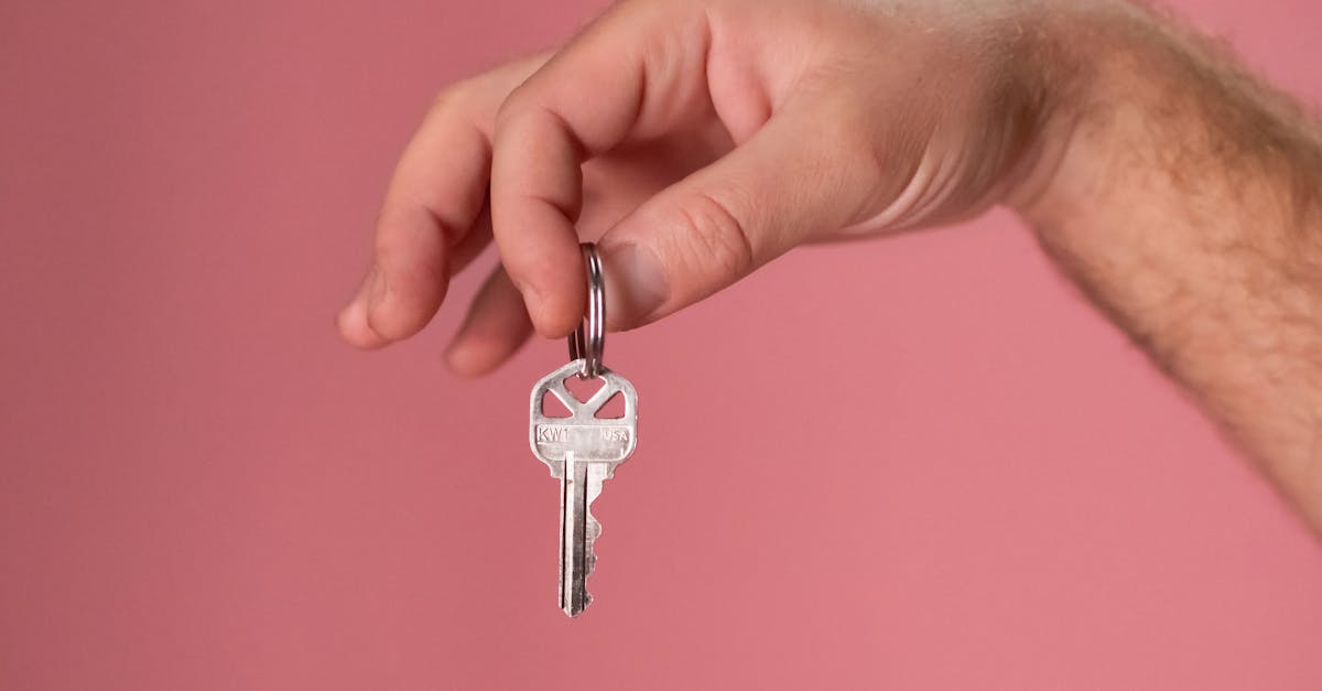 Hand holding a silver key with a pink background, symbolizing new home ownership.